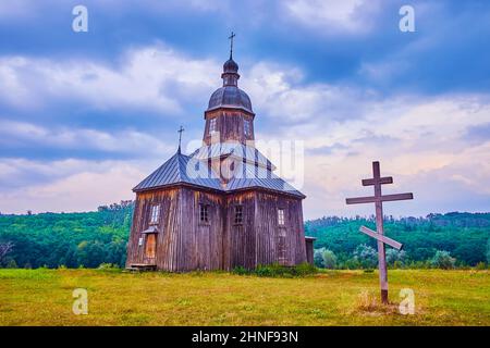 Erhaltene historische Holzkirche des Heiligen Nikolaus und ein Kreuz im historischen Kosakendorf Scansen im Dorf Stetsivka, Ukraine Stockfoto