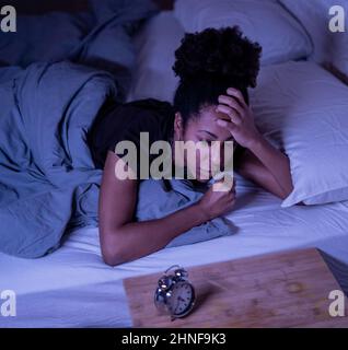 Schlaflos und verzweifelt schöne afro amerikanische Frau wach in der Nacht nicht in der Lage zu schlafen Blick auf Uhr leiden an Schlaflosigkeit in Schlafstörungen und Stockfoto