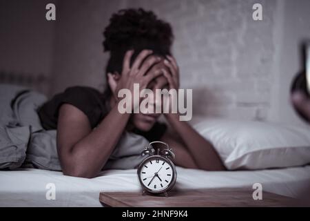 Schlaflos und verzweifelt schöne afro amerikanische Frau wach in der Nacht nicht in der Lage zu schlafen Blick auf Uhr leiden an Schlaflosigkeit in Schlafstörungen und Stockfoto