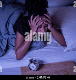 Schlaflos und verzweifelt schöne afro amerikanische Frau wach in der Nacht nicht in der Lage zu schlafen Blick auf Uhr leiden an Schlaflosigkeit in Schlafstörungen und Stockfoto