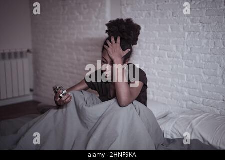 Schlaflos und verzweifelt schöne afro amerikanische Frau wach in der Nacht nicht in der Lage zu schlafen Blick auf Uhr leiden an Schlaflosigkeit in Schlafstörungen und Stockfoto