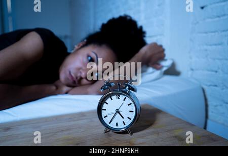Schlaflos und verzweifelt schöne afro amerikanische Frau wach in der Nacht nicht in der Lage zu schlafen Blick auf Uhr leiden an Schlaflosigkeit in Schlafstörungen und Stockfoto