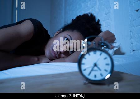 Schlaflos und verzweifelt schöne afro amerikanische Frau wach in der Nacht nicht in der Lage zu schlafen Blick auf Uhr leiden an Schlaflosigkeit in Schlafstörungen und Stockfoto