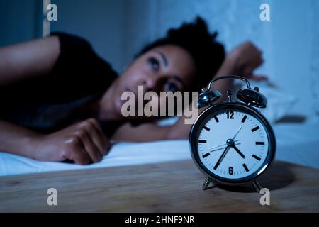 Schlaflos und verzweifelt schöne afro amerikanische Frau wach in der Nacht nicht in der Lage zu schlafen Blick auf Uhr leiden an Schlaflosigkeit in Schlafstörungen und Stockfoto