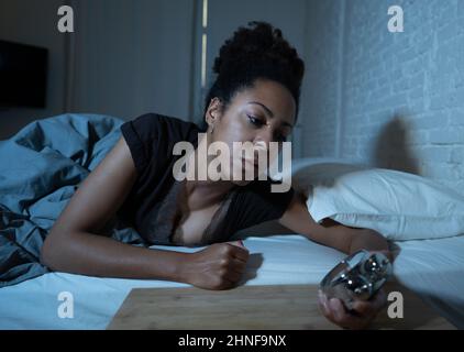 Schlaflos und verzweifelt schöne afro amerikanische Frau wach in der Nacht nicht in der Lage zu schlafen Blick auf Uhr leiden an Schlaflosigkeit in Schlafstörungen und Stockfoto