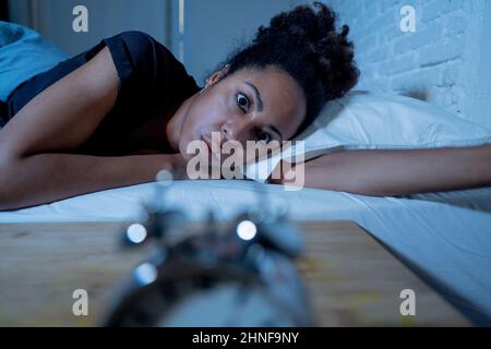Schlaflos und verzweifelt schöne afro amerikanische Frau wach in der Nacht nicht in der Lage zu schlafen Blick auf Uhr leiden an Schlaflosigkeit in Schlafstörungen und Stockfoto