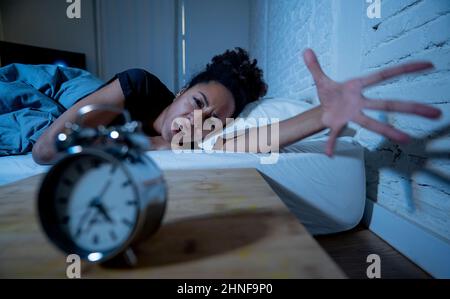 Schlaflos und verzweifelt schöne afro amerikanische Frau wach in der Nacht nicht in der Lage zu schlafen Blick auf Uhr leiden an Schlaflosigkeit in Schlafstörungen und Stockfoto