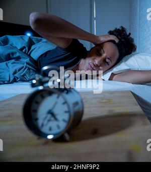 Schlaflos und verzweifelt schöne afro amerikanische Frau wach in der Nacht nicht in der Lage zu schlafen Blick auf Uhr leiden an Schlaflosigkeit in Schlafstörungen und Stockfoto
