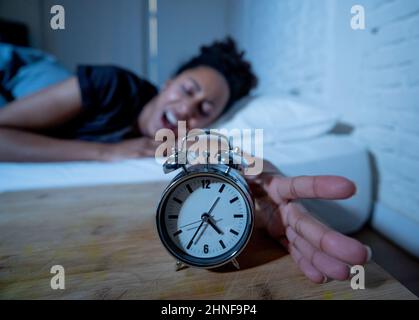 Schlaflos und verzweifelt schöne afro amerikanische Frau wach in der Nacht nicht in der Lage zu schlafen Blick auf Uhr leiden an Schlaflosigkeit in Schlafstörungen und Stockfoto
