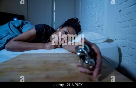 Schlaflos und verzweifelt schöne afro amerikanische Frau wach in der Nacht nicht in der Lage zu schlafen Blick auf Uhr leiden an Schlaflosigkeit in Schlafstörungen und Stockfoto