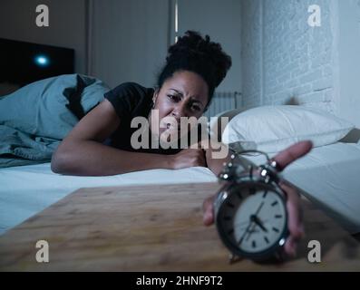Schlaflos und verzweifelt schöne afro amerikanische Frau wach in der Nacht nicht in der Lage zu schlafen Blick auf Uhr leiden an Schlaflosigkeit in Schlafstörungen und Stockfoto