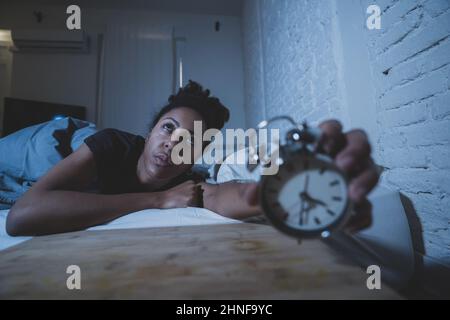 Schlaflos und verzweifelt schöne afro amerikanische Frau wach in der Nacht nicht in der Lage zu schlafen Blick auf Uhr leiden an Schlaflosigkeit in Schlafstörungen und Stockfoto