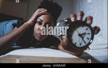 Schlaflos und verzweifelt schöne afro amerikanische Frau wach in der Nacht nicht in der Lage zu schlafen Blick auf Uhr leiden an Schlaflosigkeit in Schlafstörungen und Stockfoto