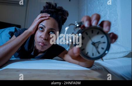 Schlaflos und verzweifelt schöne afro amerikanische Frau wach in der Nacht nicht in der Lage zu schlafen Blick auf Uhr leiden an Schlaflosigkeit in Schlafstörungen und Stockfoto