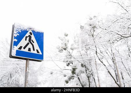 Gefrorenes Fußgängerschild, das an einem frostigen, verschneiten Tag mit Schnee bedeckt ist Stockfoto