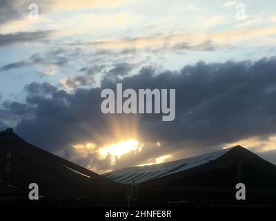 Dramatische Sonnenstrahlen, die durch dunkle Wolken über Dächern brechen Stockfoto