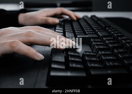 Nahaufnahme der Frau, die auf der Computertastatur tippt und auf dem Tisch im Internet surft. Stockfoto
