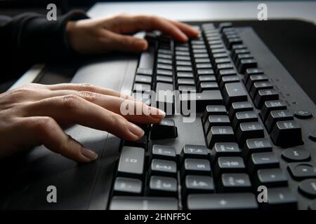 Nahaufnahme der Frau, die auf der Computertastatur tippt und auf dem Tisch im Internet surft. Stockfoto