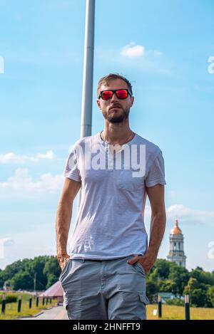 Stilvoller junger Mann mit Sonnenbrille und Händen in den Taschen Stockfoto
