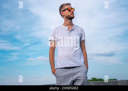 Schöner junger Mann mit den Händen in den Taschen gegen den wolkigen Himmel Stockfoto