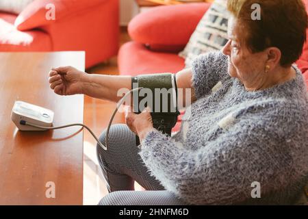 Ältere Frau, die die Kompressionsmanschette eines Blutdruckmonitors auflegt. Stockfoto