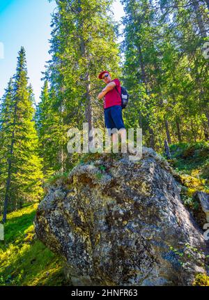 Der junge Reisende Tourist steht auf einem riesigen Felsen in der natürlichen norwegischen Landschaft in Hemsedal Viken Norwegen. Stockfoto