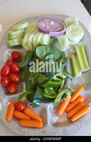 Eine silberne Platte mit buntem, rohem, biologischem Spinat, Gurken, Pflaumentomaten, Rote Zwiebeln, Babykarotten, Sellerie und grüne Paprika Stockfoto