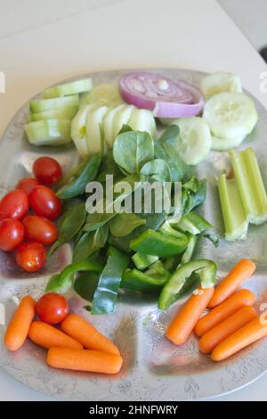 Eine silberne Platte mit rohem, biologischem Spinat, Gurken, Pflaumentomaten, roten Zwiebeln, Baby Karotten, Sellerie und grüne Paprika, ein Vegeta Stockfoto