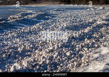 Schnee, Frost und Wind erzeugen unregelmäßig geformte Eisbälle am Ufer des Lake Michigan Stockfoto