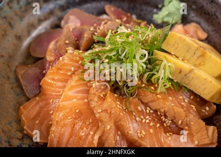 Nahaufnahme, Schale mit japanischem Maguro, Thunfisch und Lachs-Reis auf der Oberseite mit japanischem gerolltem Omelett und Zwiebel. Stockfoto