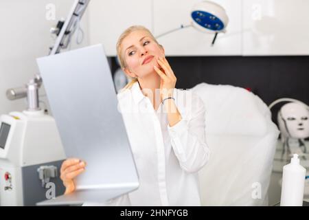 Glückliche Frau, die ihr Gesicht nach kosmetologischen Eingriffen in der Klinik untersucht Stockfoto