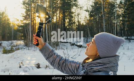 Frau, die auf einem Handheld-Film hält 3-Achsen-Gimbal-Stabilisiergerät im Winter für Smartphone. Girl Blogger Make Selfie, Broadcast Video Blogging, Vlogging. Videograf Operator Nimmt Fotovideo Auf. Stockfoto