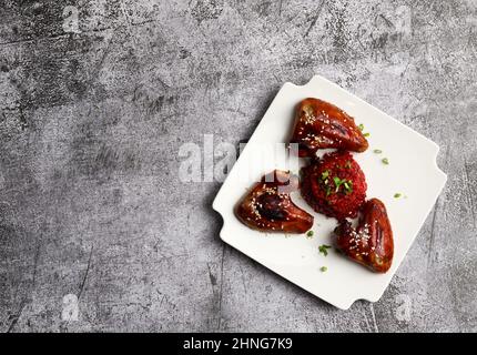 Gebratene Hähnchenflügel mit Rote Beete Risotto auf einem quadratischen Teller auf dunkelgrauem Hintergrund. Draufsicht, flach liegend Stockfoto