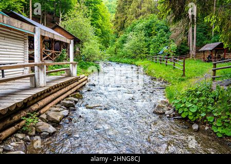Holzschuppen neben einem kleinen Bach, umgeben von grünen Bäumen im Wald Stockfoto