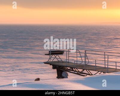 Bank auf dem Pier am gefrorenen Stausee. Winterabend Goldener Himmel bei Sonnenuntergang, schneebedeckte Ebene, gefrorener Nowosibirsk Stausee am ob Fluss in der Nähe von Nowosib Stockfoto