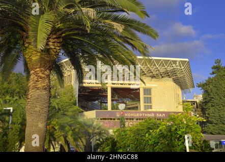 Sotschi, Russland - 11.01.2021: "Festival Concert Hall" unter Palmen. Die Fassade eines Gebäudes mit einem strukturellen Dach von der Meerseite unter einem blauen s Stockfoto