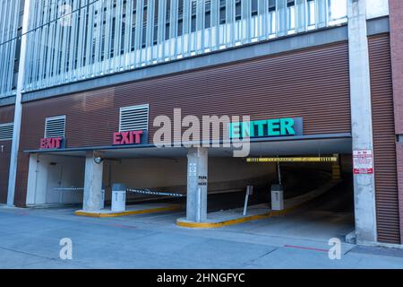 Zwei Rampen für die Parkgarage, ein- und Ausgänge mit blauen und roten Schildern über Türen, an denen Autos das Gebäude betreten und verlassen. Stockfoto