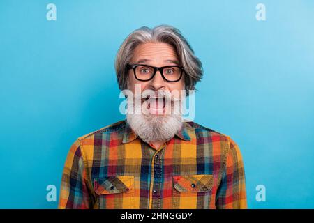 Foto von beeindruckt lustig pensionierten Mann tragen karierte Hemd Brille offenen Mund isoliert blauen Hintergrund Stockfoto