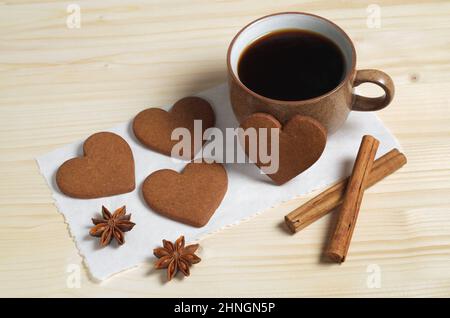 Tasse Kaffee, herzförmige Ingwerkekse, Zimt und Anisstern auf einem Holztisch Stockfoto