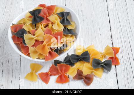 Bunte Pasta in Form einer Schleife in einer Schüssel auf weißem Holztisch aus nächster Nähe Stockfoto