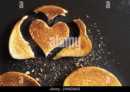 Stück gebratenes Brot in Herzform und Scheiben mit Krümel auf schwarzem, altem Metallic-Hintergrund, Draufsicht Stockfoto