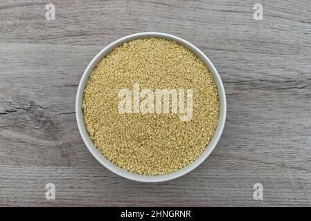 Schale aus rohem Couscous isoliert auf Holzhintergrund. Draufsicht. Stockfoto