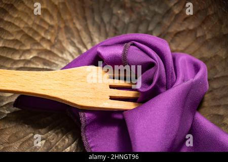 Holzgabel mit purpurfarbenem Satin auf einer Platte aus dunklem Holz Stockfoto