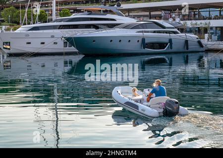 Mann und Hund segeln auf dem Gummiboot in Richtung der Yacht im Hafen, Sommerurlaub Thema Stockfoto