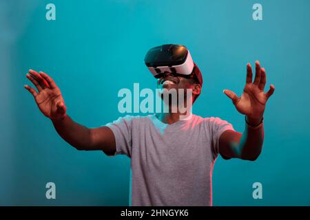 Fröhliche Erwachsene schauen nach oben und genießen vr Brillen Erfahrung, spielen mit Virtual-Reality-Brille zu sehen 3D visuelle Simulation. Modell für Männer, das ein modernes Headset trägt, um futuristische Technologie zu nutzen. Stockfoto