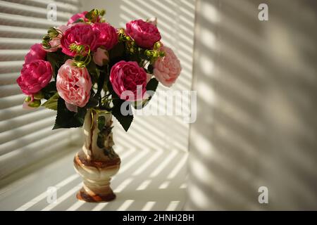 Rosa Pfingstrosen-Blüten in Vase auf sonniger Fensterbank. Stockfoto