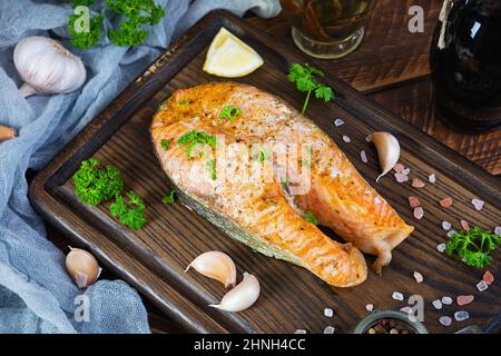 Gebackenes Lachssteak mit Kräutern auf Holzschneidebrett. Gegrillter Lachs mit Salz und Pfeffer Stockfoto
