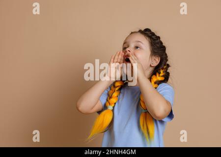 Junges ängstliches Mädchen, das mit geöffnetem Mund schrie und die Hände am Mund hielt und jemanden um Hilfe bat, Kanekalon-Zöpfe der gelben Farbe zu haben, die aussehen Stockfoto