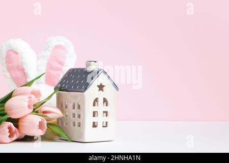 Osterkomposition. Tulpe Blumen Kaninchen Ohren Spielzeug Haus auf rosa Hintergrund kopieren Raum Stockfoto