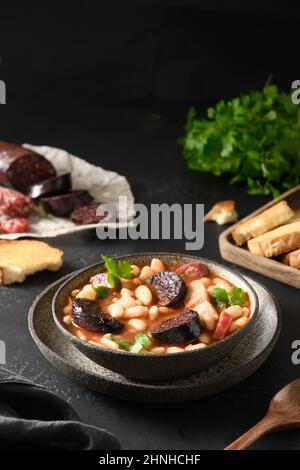 Asturiana fabada mit Chorizo, Speck, Wurst, Haricot serviert frischen knusprigen Toast auf schwarzem Tisch. Vertikale Ausrichtung. Leckere traditionelle spanische Warmi Stockfoto